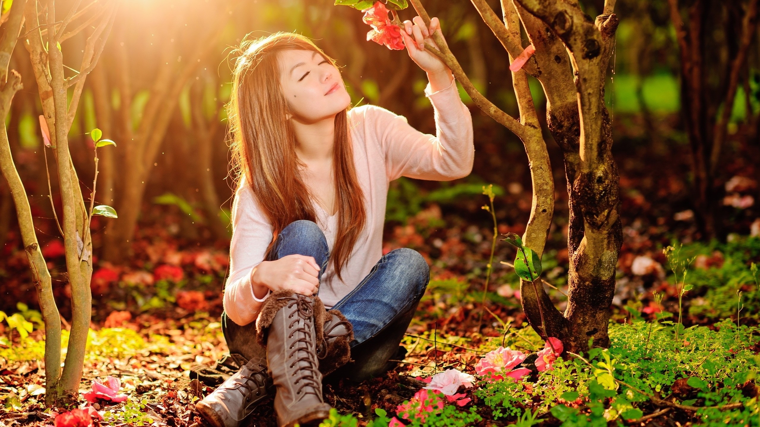 People 2560x1440 women model brunette long hair nature trees forest closed eyes women outdoors sitting Asian smiling flowers sunlight boots jeans backlighting