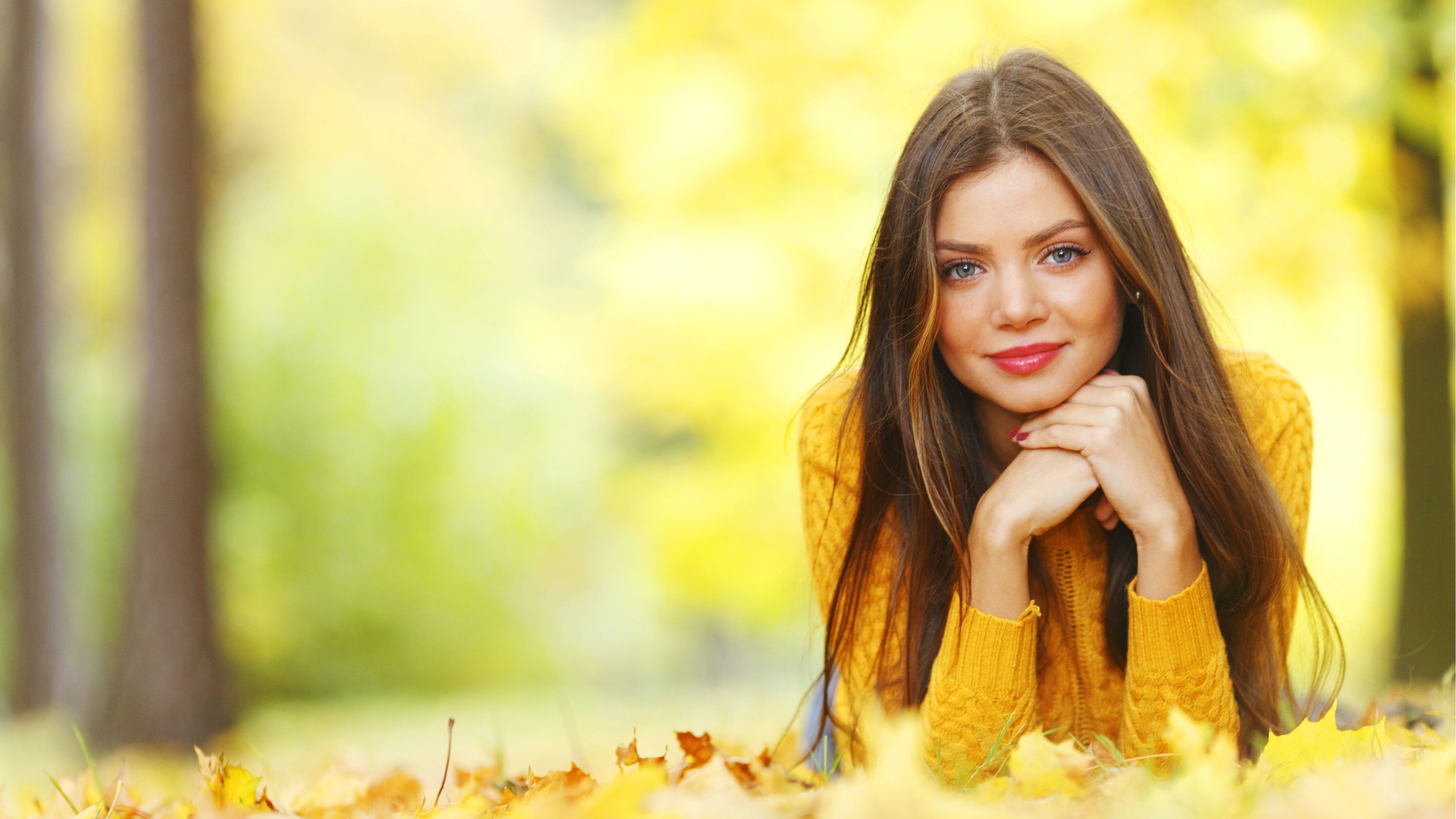People 3840x2160 women model brunette long hair women outdoors nature face portrait trees smiling blue eyes red lipstick sweater leaves fall depth of field lying on front looking at viewer yellow sweater yellow clothing red nails