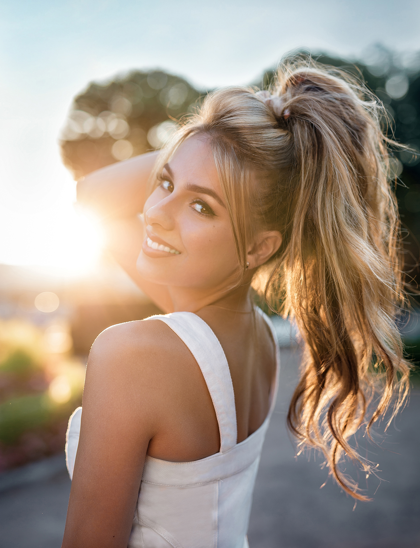 People 1474x1920 Aleksandr Smirnov women blonde long hair ponytail wavy hair hands in hair makeup eyeliner looking at viewer lipstick smiling white clothing sunlight bright lens flare Sun looking back tanned