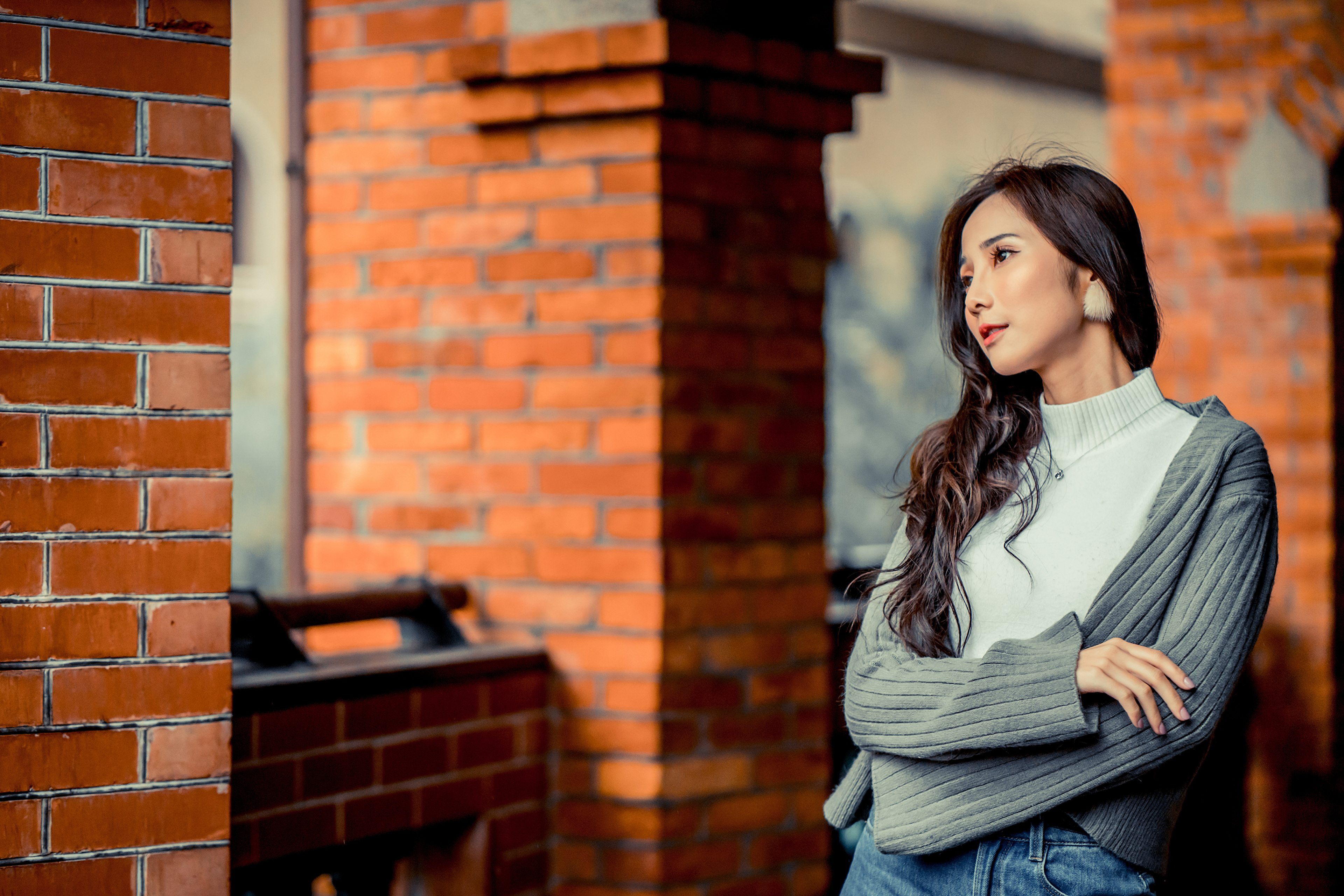 People 3840x2561 Asian women model long hair brunette depth of field bricks column pullover jacket jeans feather earrings necklace looking into the distance