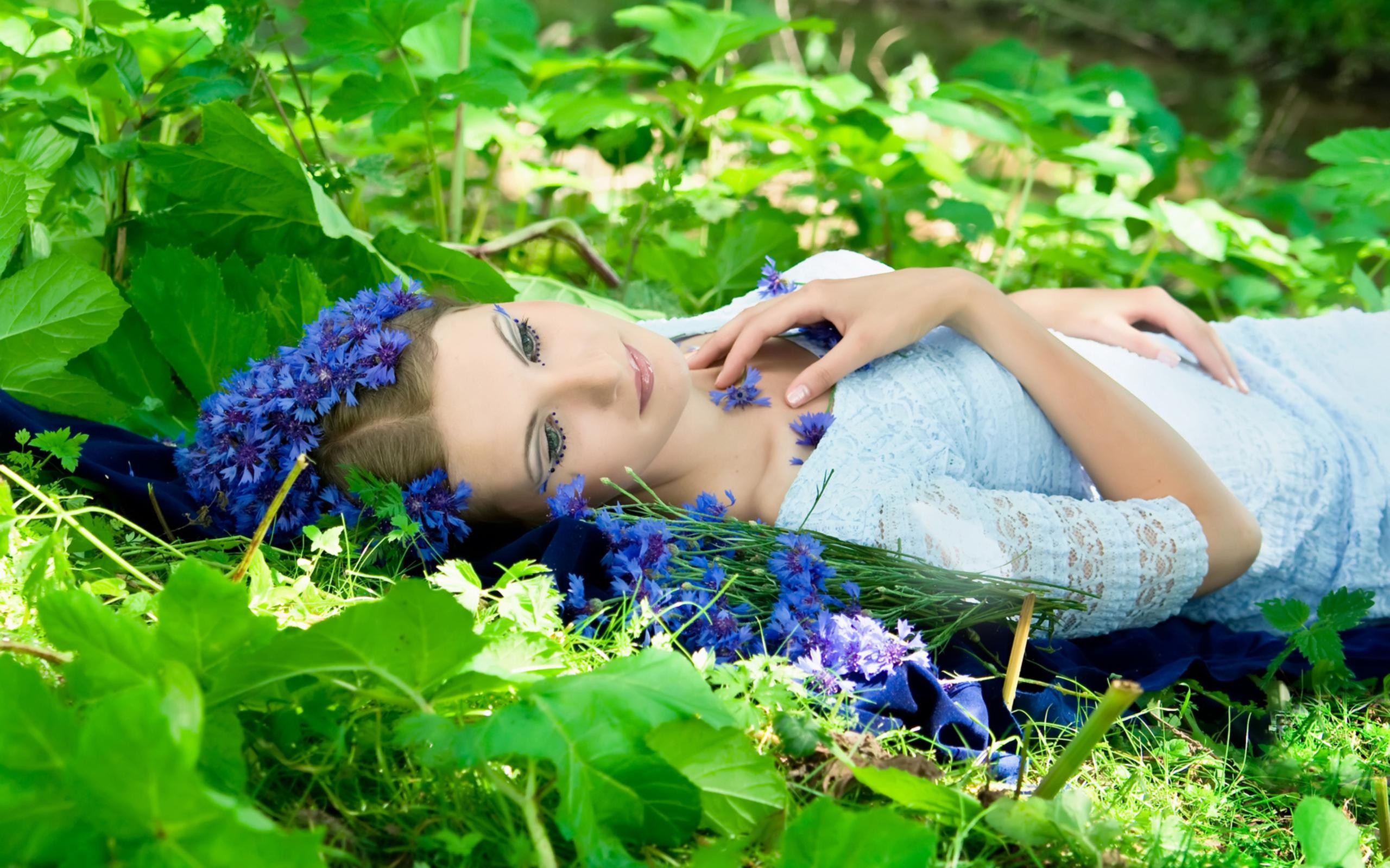 People 2560x1600 women model brunette face women outdoors lying on back nature flowers leaves makeup dress sunlight blue flowers fantasy girl grass plants cyan clothing flower crown lipstick