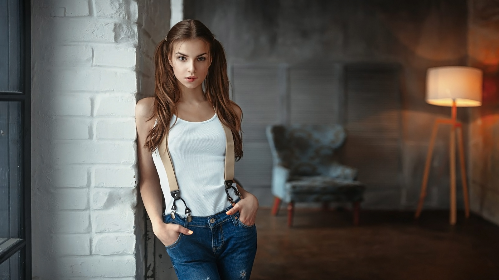 People 1600x900 Georgy Chernyadyev women brunette twintails long hair straight hair makeup looking at viewer biting lips tank top white clothing suspenders hands in pockets jeans denim wall warm light depth of field Elina Loseva