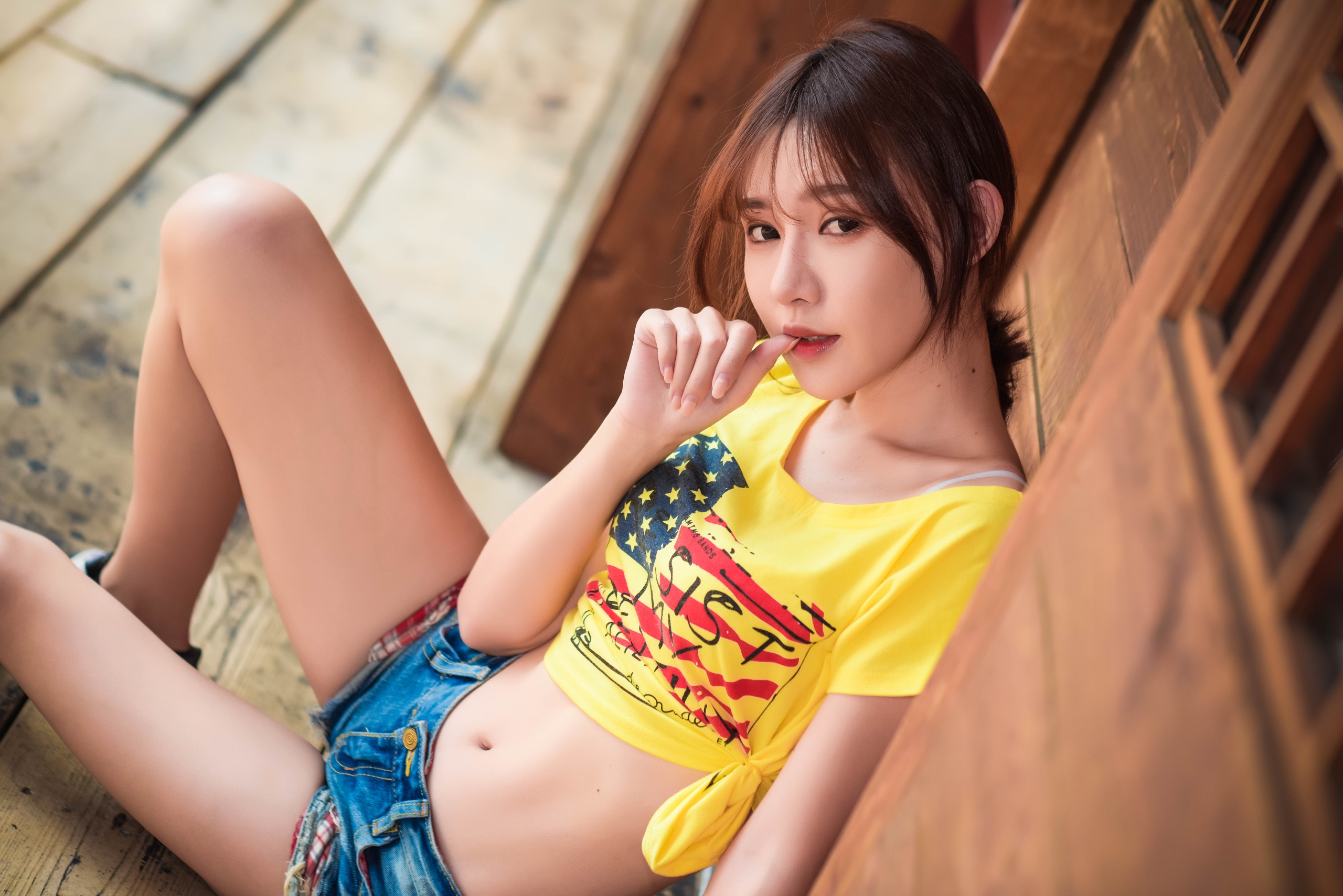 People 2560x1709 women model Asian brunette ponytail looking at viewer finger on lips T-shirt yellow t-shirt belly jean shorts denim wood sitting portrait outdoors women outdoors high angle