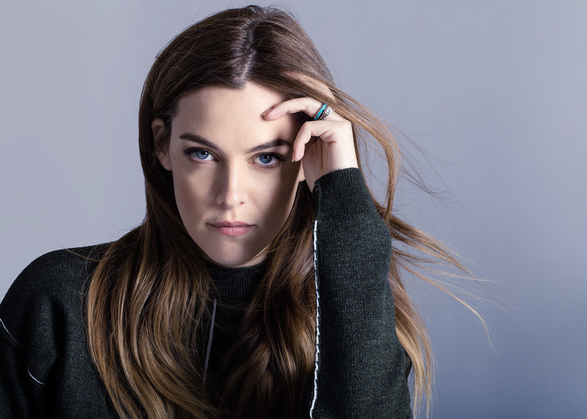 People 1946x1390 Riley Keough actress blue eyes brunette long hair looking at viewer simple background sweater black sweater touching face gray background makeup women