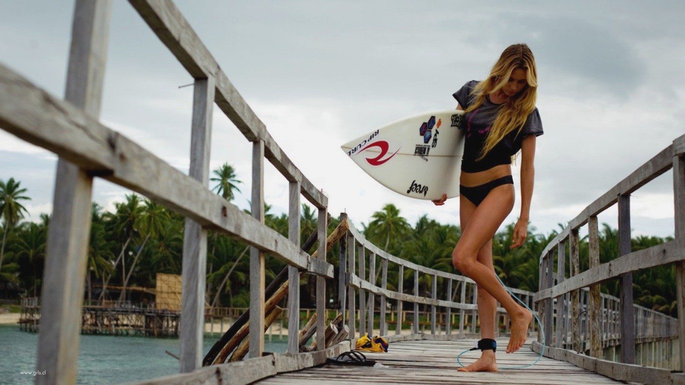 People 1366x768 women Alana Blanchard blonde bikini bottoms T-shirt depth of field surfers surfboards watermarked standing standing on one leg outdoors