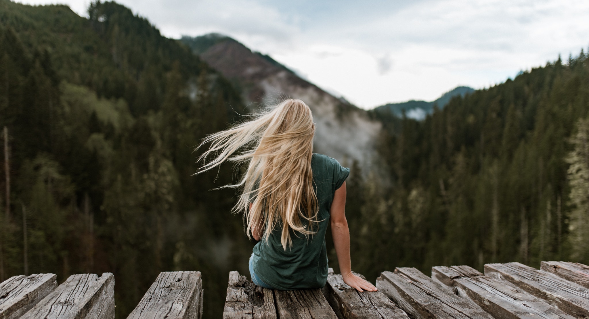 People 2048x1110 women blonde sitting women outdoors mountains T-shirt depth of field back long hair windy