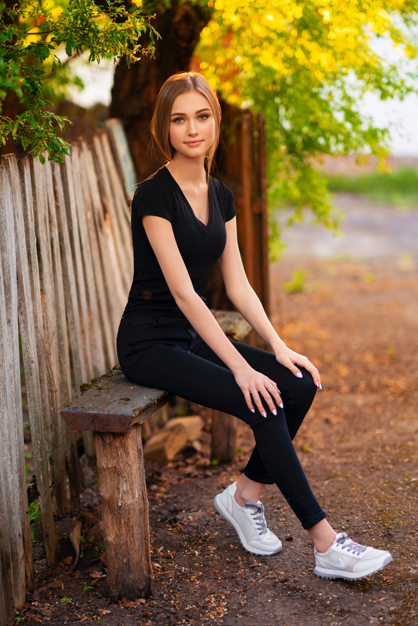 People 1366x2048 Olga Boyko women brunette looking at viewer smiling black clothing sneakers bench trees sunlight Angelina Diachenko model women outdoors black t-shirt black pants hand on leg fence on bench white shoes closed mouth portrait display