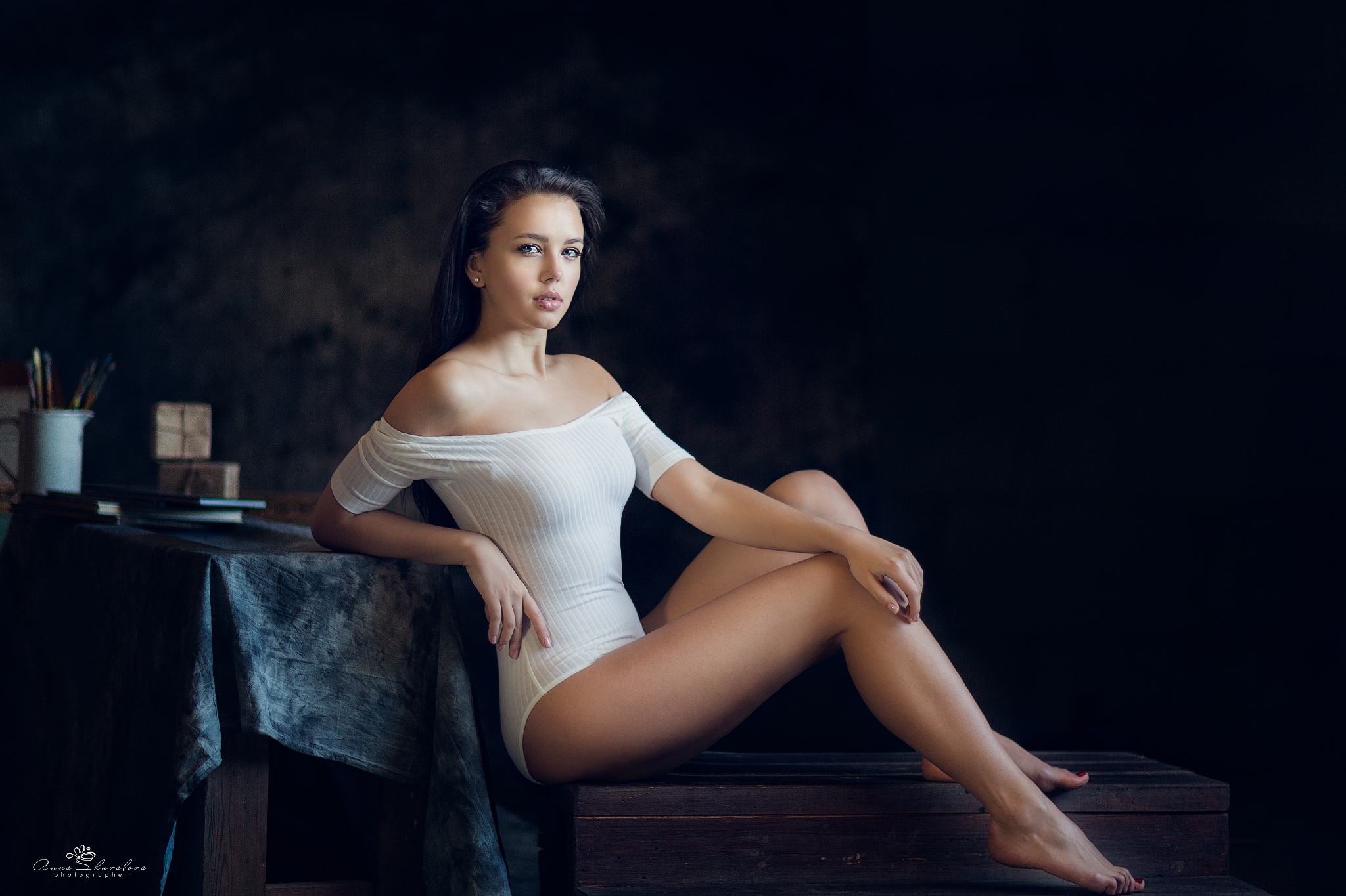 People 2048x1365 women model Anna Shuvalova brunette long hair looking at viewer bare shoulders bodysuit sitting barefoot dark background indoors women indoors frontal view on bench hand on leg off shoulder hands on knees painted toenails