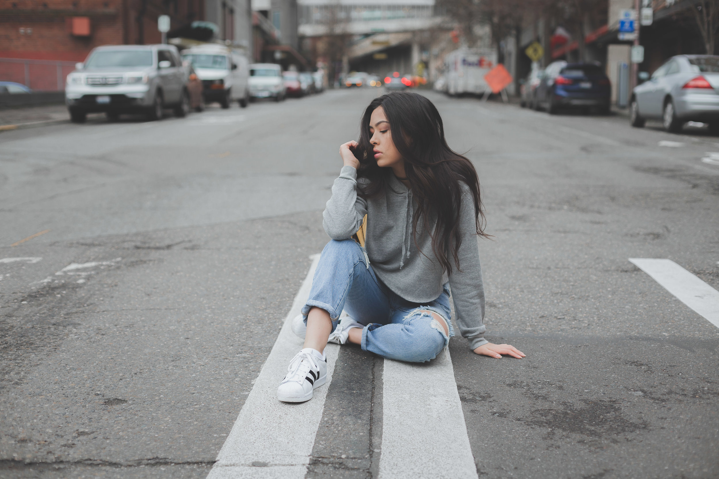 People 2500x1667 women model outdoors torn jeans sneakers street sweatshirts long hair on the floor brunette torn clothes touching hair urban