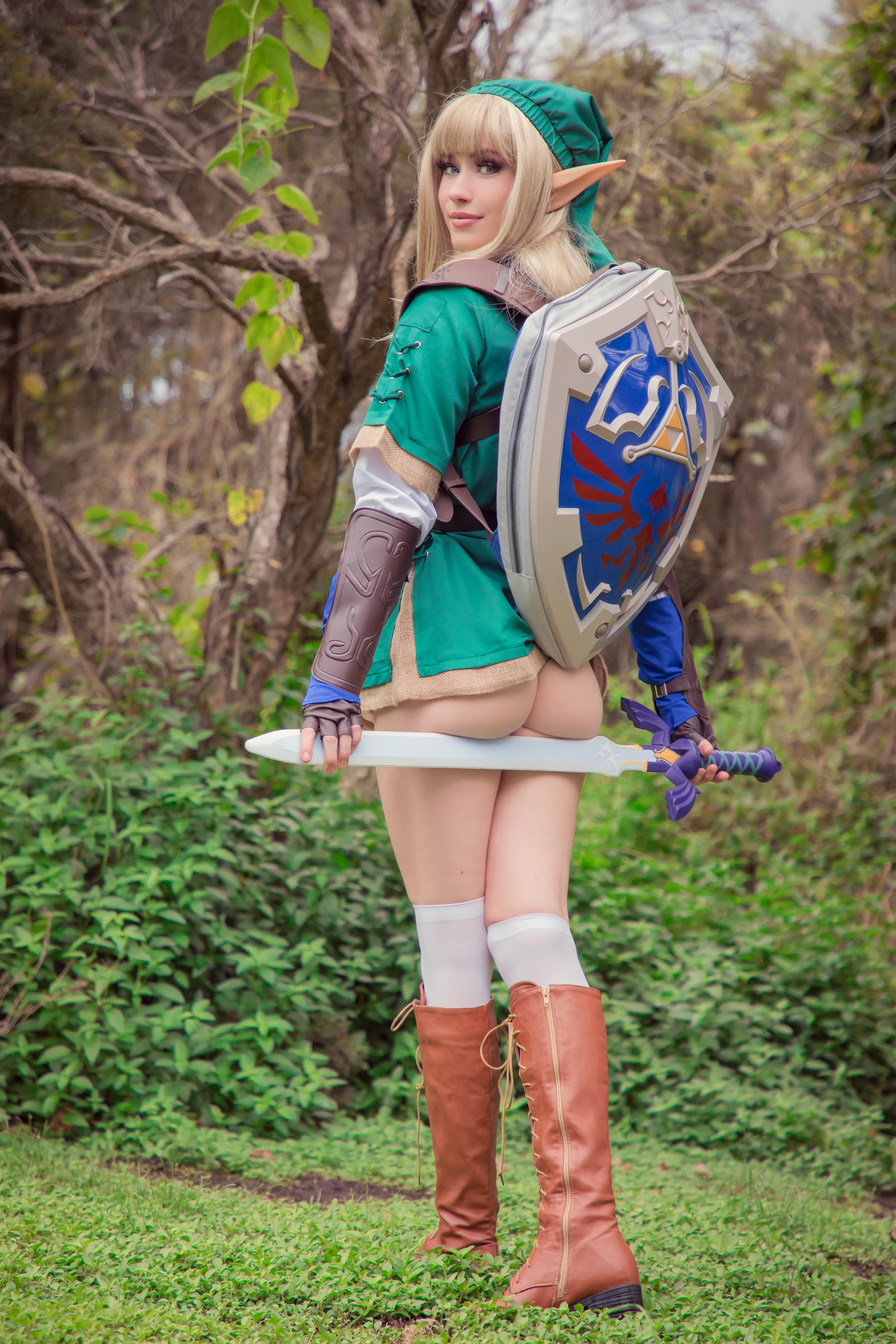 People 4480x6720 Nichameleon women model cosplay Link The Legend of Zelda video games sword video game characters dress blonde pointy ears elves looking at viewer blue eyes ass knee-highs boots behind forest portrait display outdoors women outdoors genderswap butt floss white stockings green tunic
