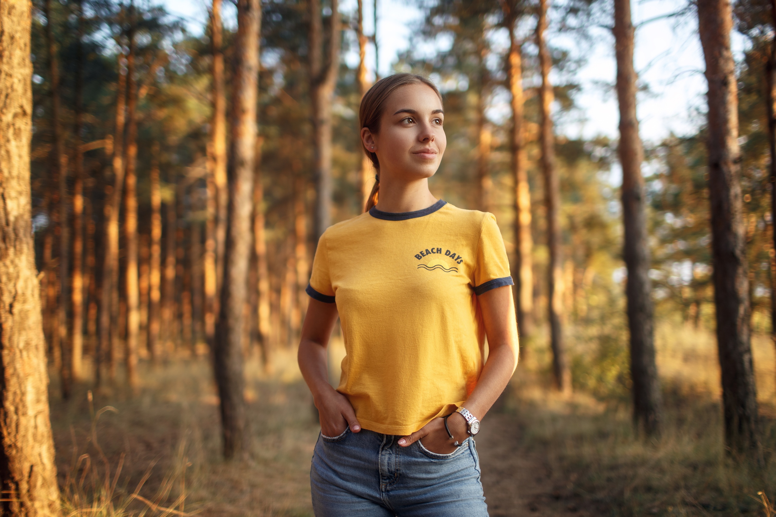 People 2560x1706 women model ponytail looking away brown eyes T-shirt jeans hands in pockets watch trees forest depth of field portrait outdoors women outdoors smiling wristwatch