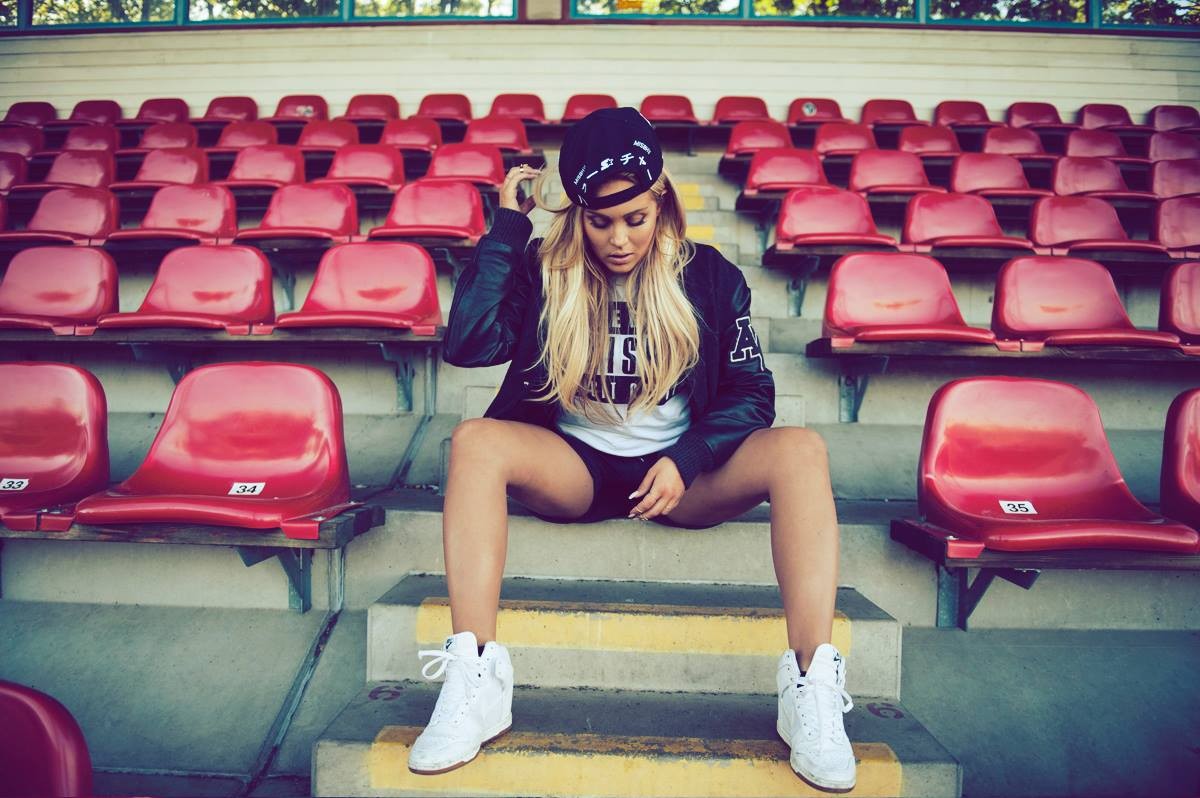 People 1200x798 women blonde sportswear long hair sneakers women outdoors sitting spread legs looking away shoes white shoes stadium hat women with hats leather jacket makeup numbers