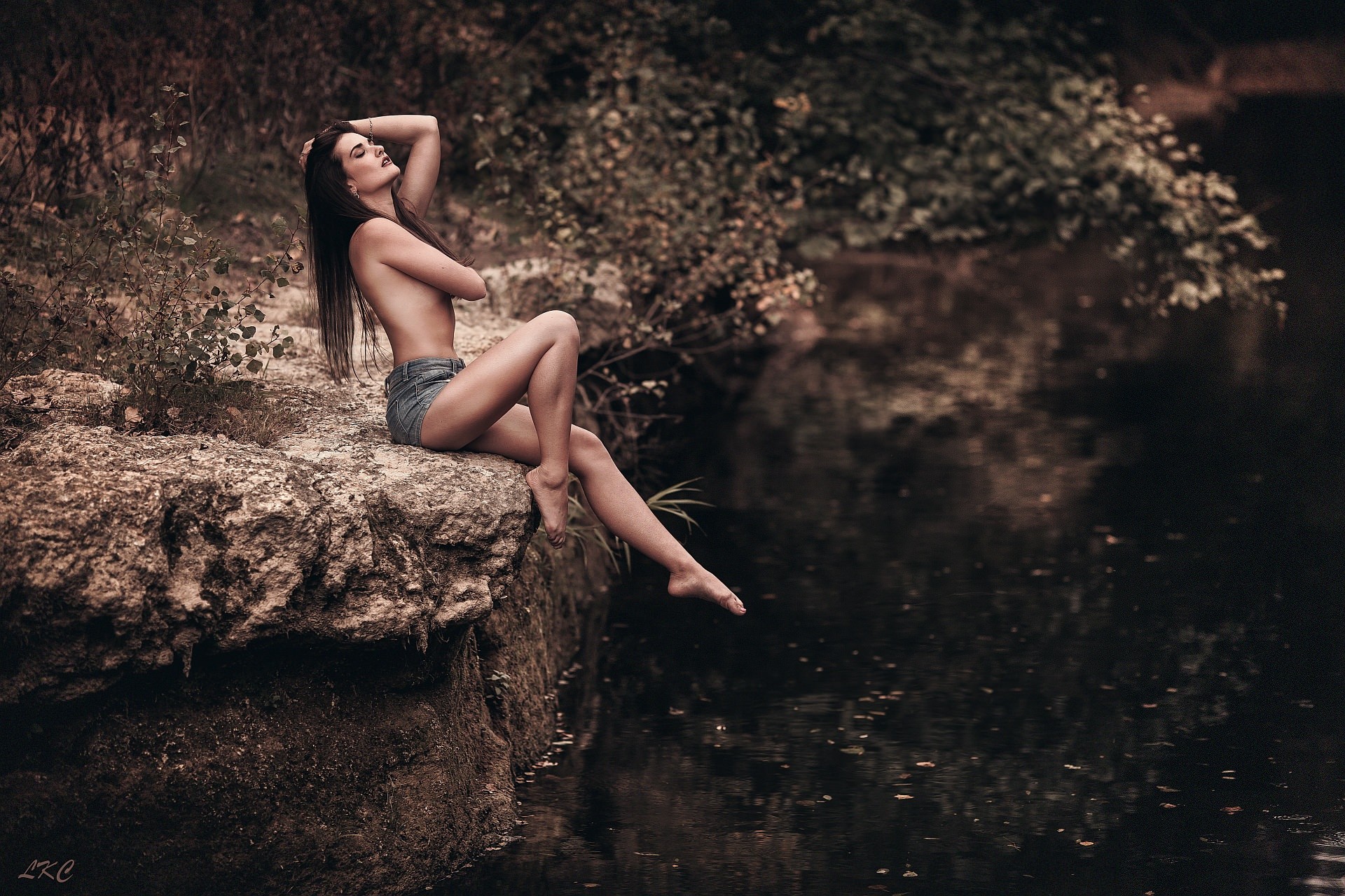 People 1920x1280 women strategic covering sitting river closed eyes jean shorts outdoors women outdoors partially clothed Laurent Kace dark hair legs thighs barefoot nature watermarked topless