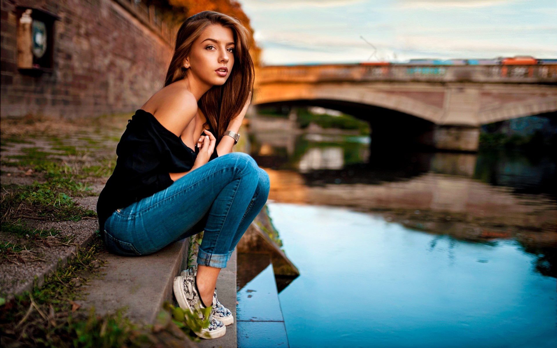 People 1920x1200 Lods Franck women model brunette long hair sneakers jeans black top strapless dress bare shoulders warm colors urban looking into the distance retouching sitting women outdoors outdoors looking at viewer makeup water no socks
