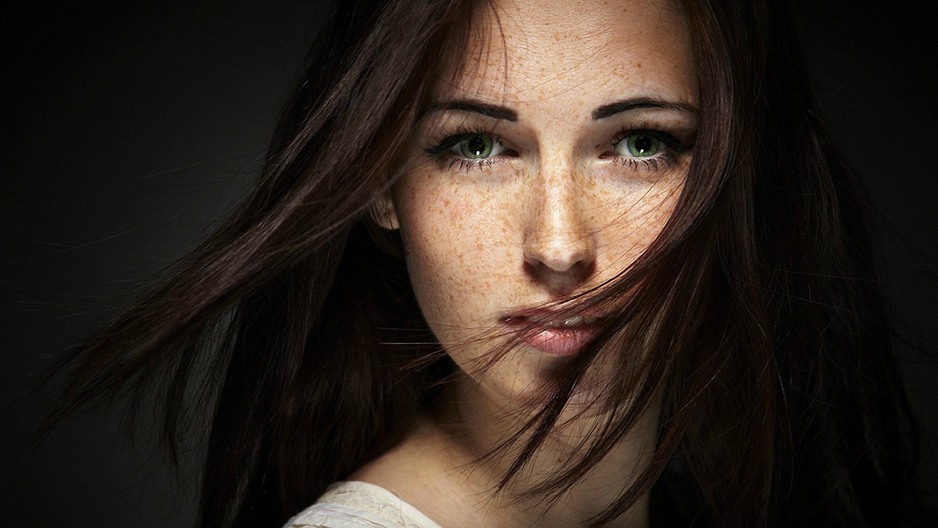 People 1920x1080 women brunette face green eyes freckles looking at viewer portrait black background long hair hair in face women indoors simple background model