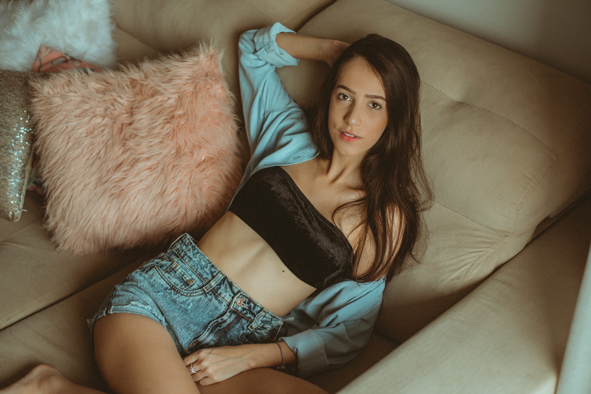 People 2000x1334 women portrait model brunette brown eyes hands in hair arms up tube top black top blue jacket jean shorts short shorts sitting couch pillow belly Junior Rossato bandeau top