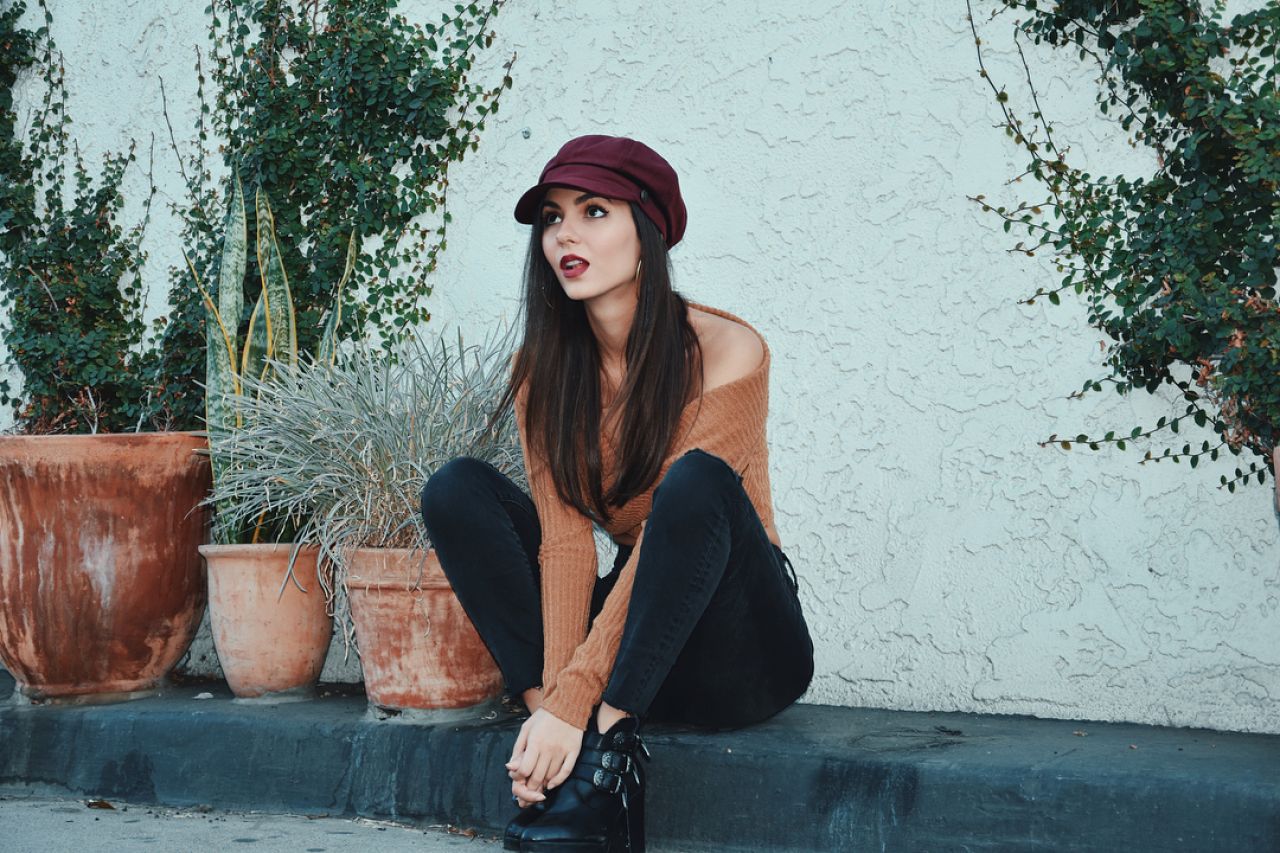 People 1280x853 Victoria Justice women actress singer brunette outdoors long hair sitting Latinas brown sweater looking up black pants black boots Red cap hoop earrings hand(s) between legs celebrity women with hats hat red lipstick