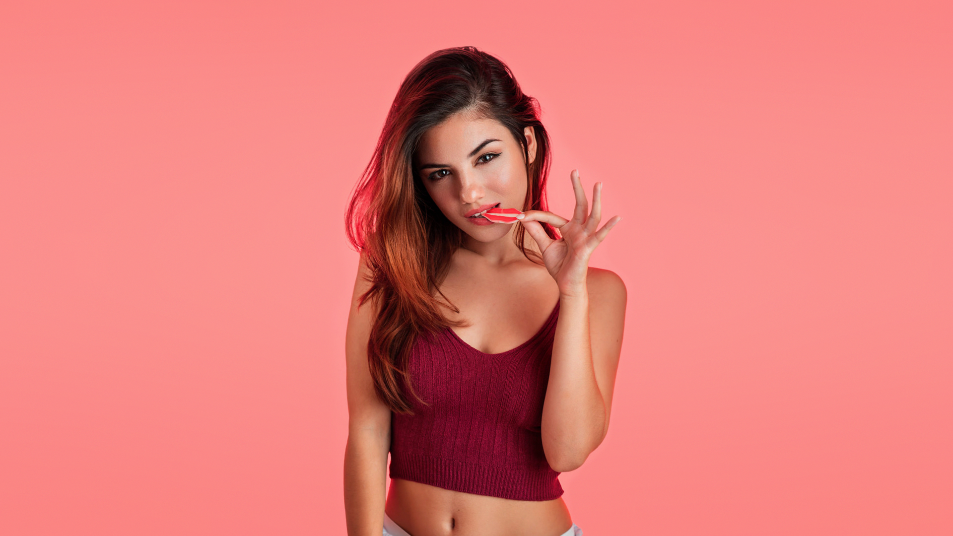 People 1920x1080 Delaia Gonzalez women model brunette portrait looking at viewer brown eyes sweets biting cleavage short tops red tops belly simple background pink background pink Gustavo Terzaghi