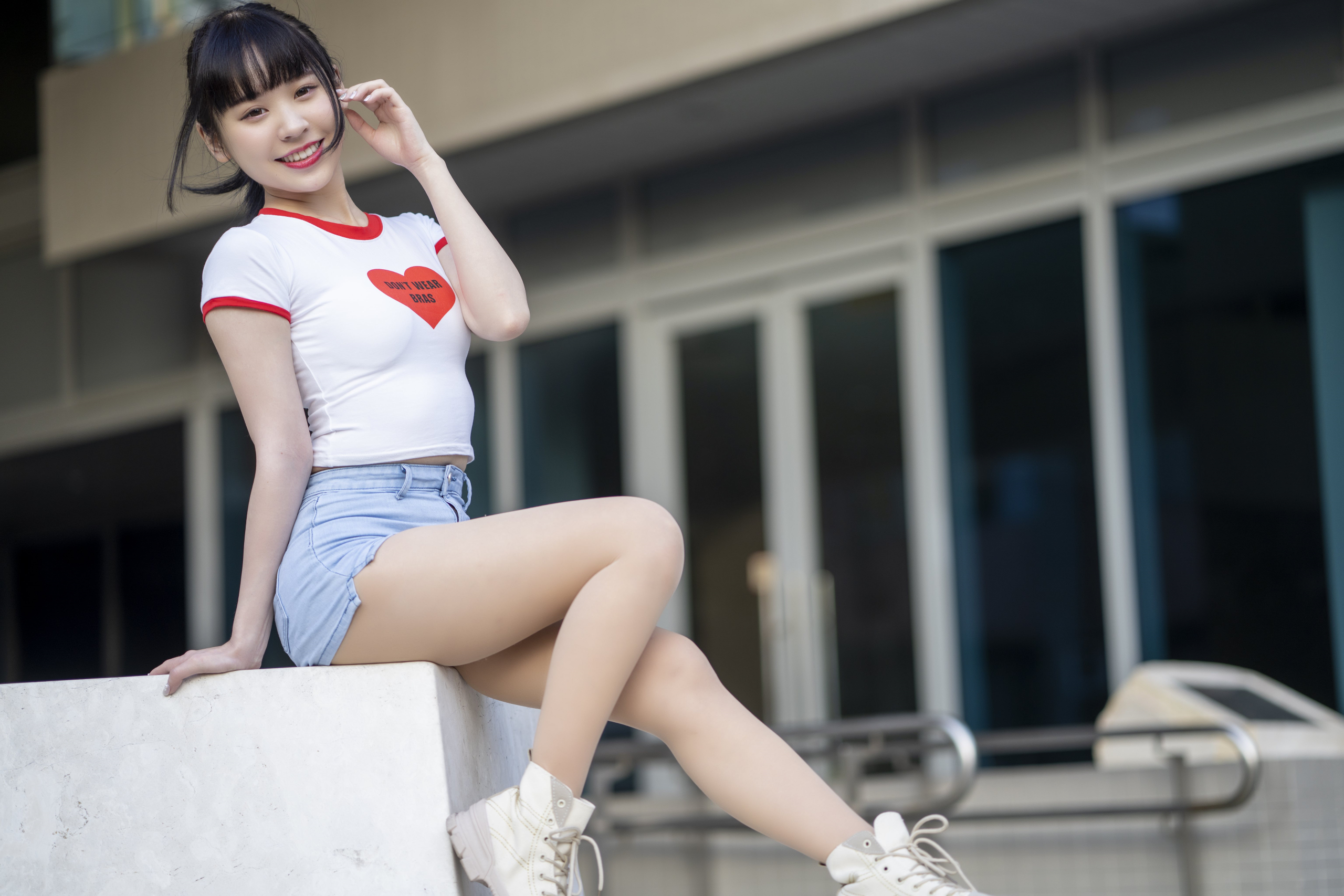 People 2560x1707 Asian women model brunette ponytail bangs looking at viewer smiling red lipstick brown eyes T-shirt jean shorts short shorts sitting street depth of field legs outdoors women outdoors heart (design) sneakers