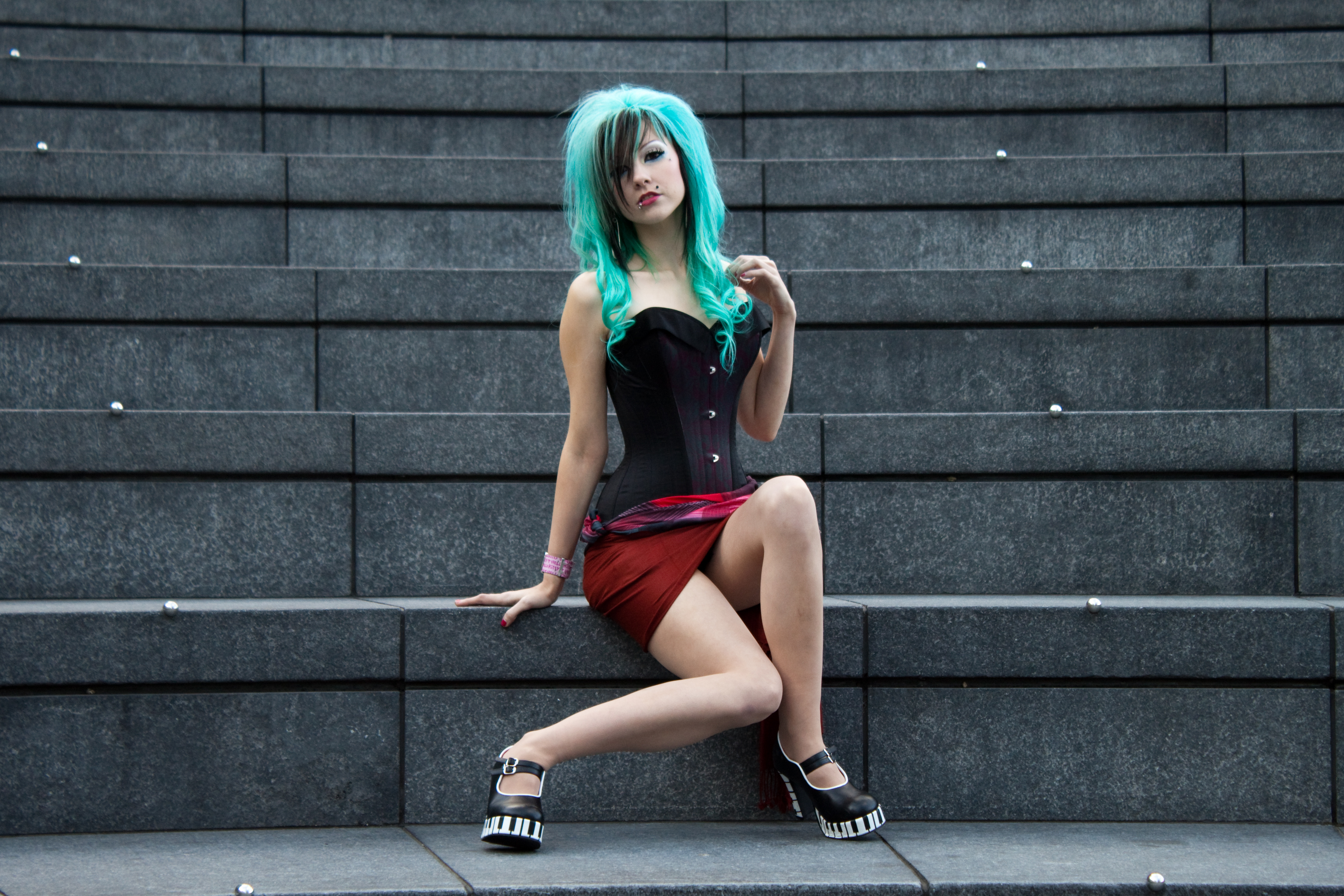 People 4593x3063 women model multi-colored hair dyed hair cyan hair piercing sitting long hair corset thighs legs heels red lipstick looking at viewer skirt red skirt Gothic