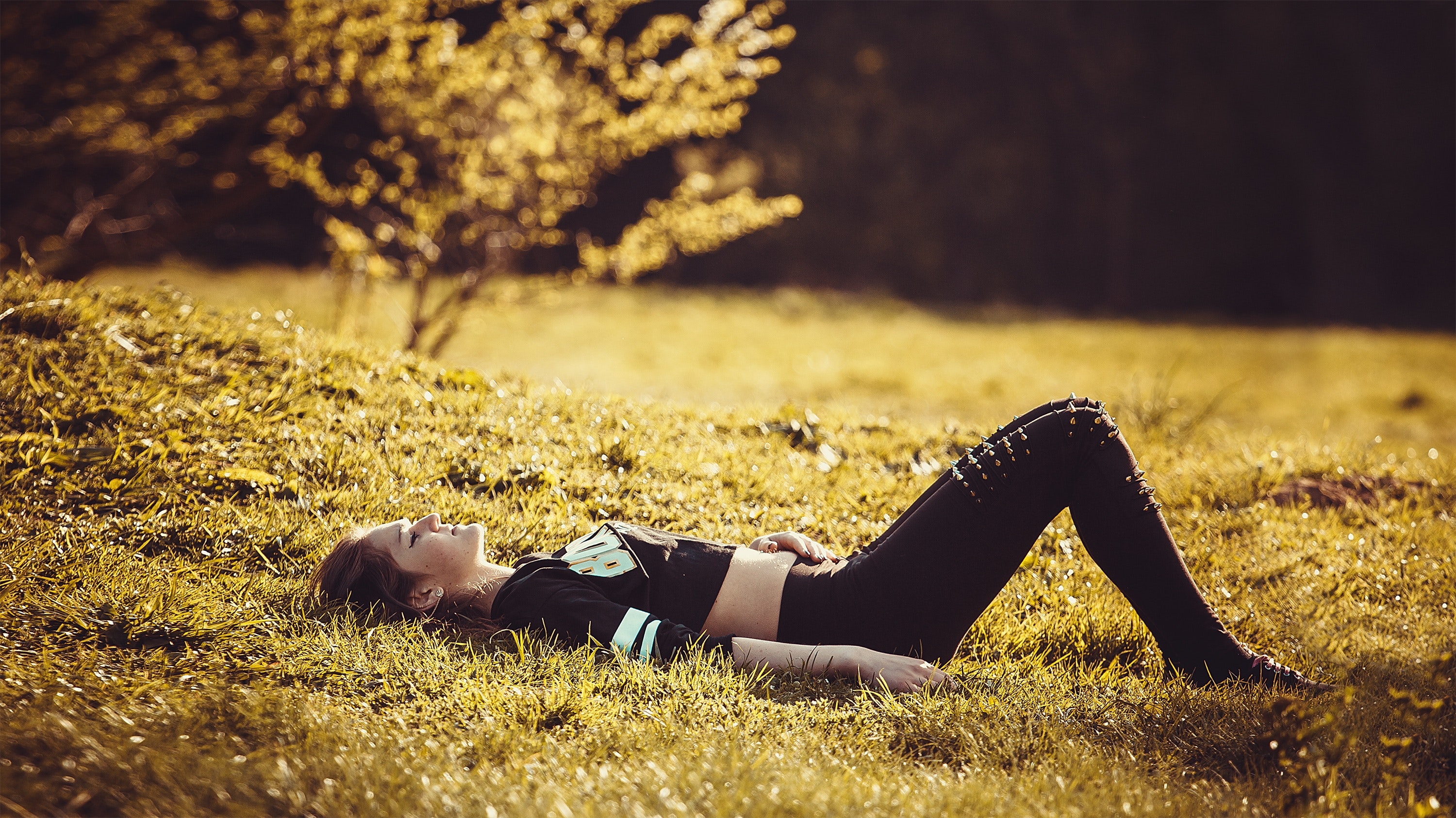 People 3000x1687 women brunette lying on back lying down grass belly spikes side view black clothing black pants crop top depth of field sunlight bare midriff