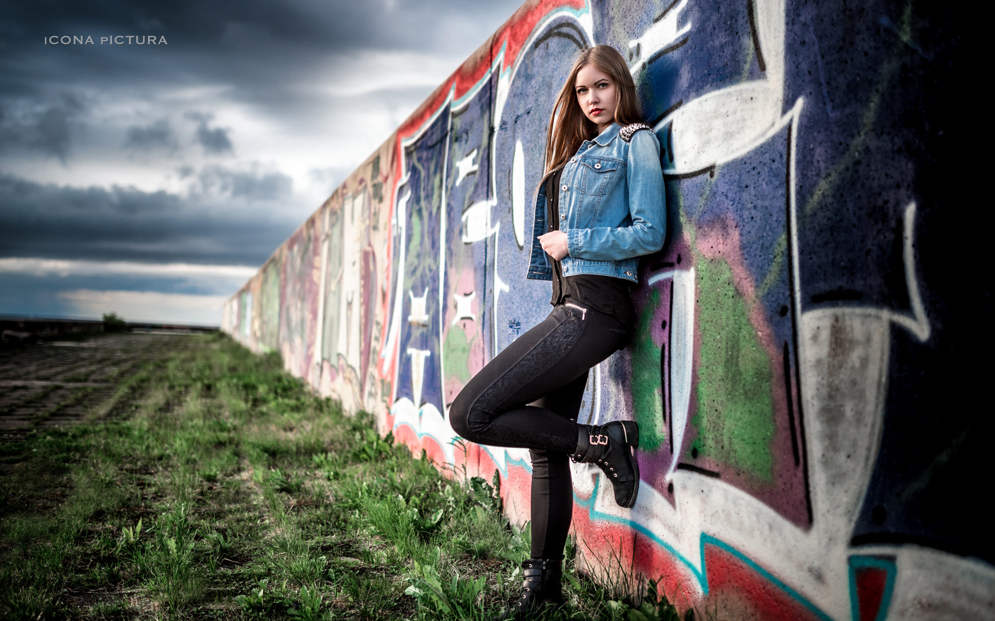 People 2000x1250 Icona Pictura women 500px photography denim jacket graffiti black pants black boots blonde long hair standing wall black shirt looking at viewer zipper jeans closed mouth standing on one leg Caucasian model women outdoors tight pants